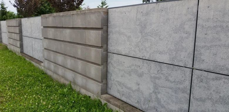 Řada betonových plotů z prefabrikovaných desek na trávníku.