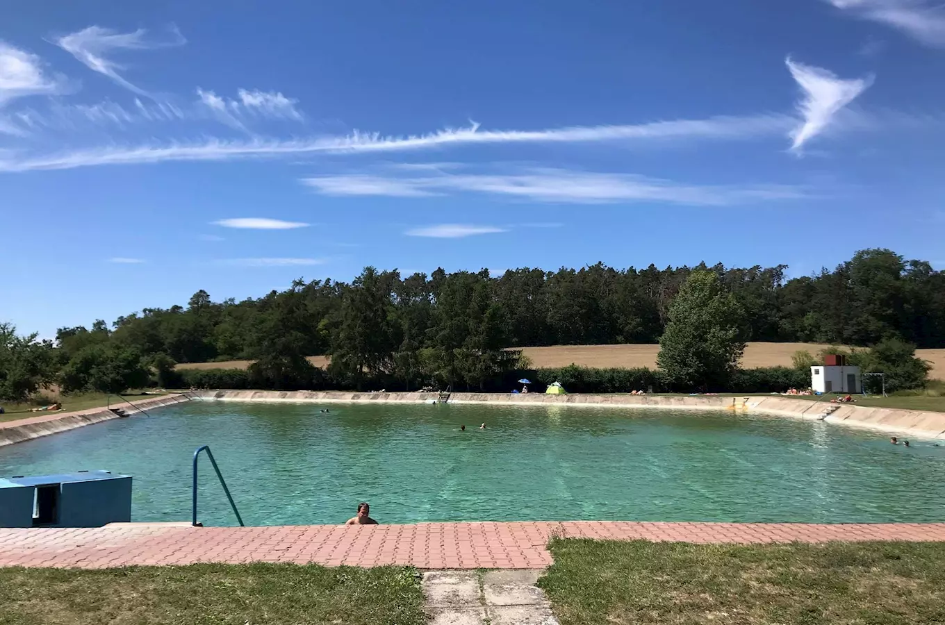 Venkovní bazén ve Všejanech s plavci pod modrou oblohou.