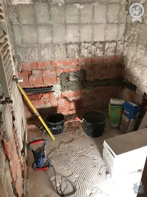 Koupelna v rekonstrukci s omítkou na zdi a dlažbou.