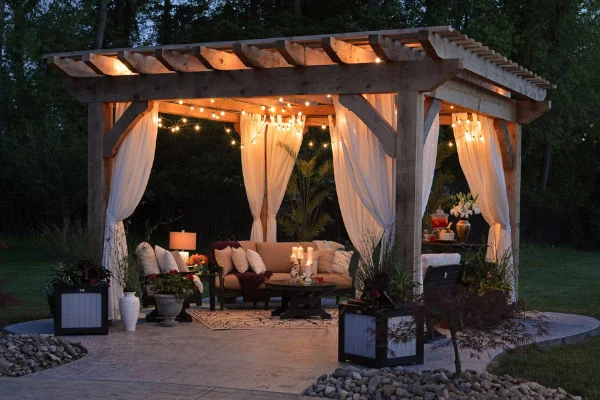 Osvětlená pergola s pohovkou a závěsy pro venkovní prostor.