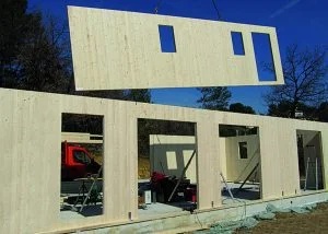 Stavba dřevěného srubu s montáží prefabrikovaného panelu na staveništi.