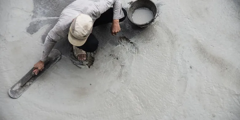 Pracovník hladí čerstvý betonovou stěrku v koupelně.