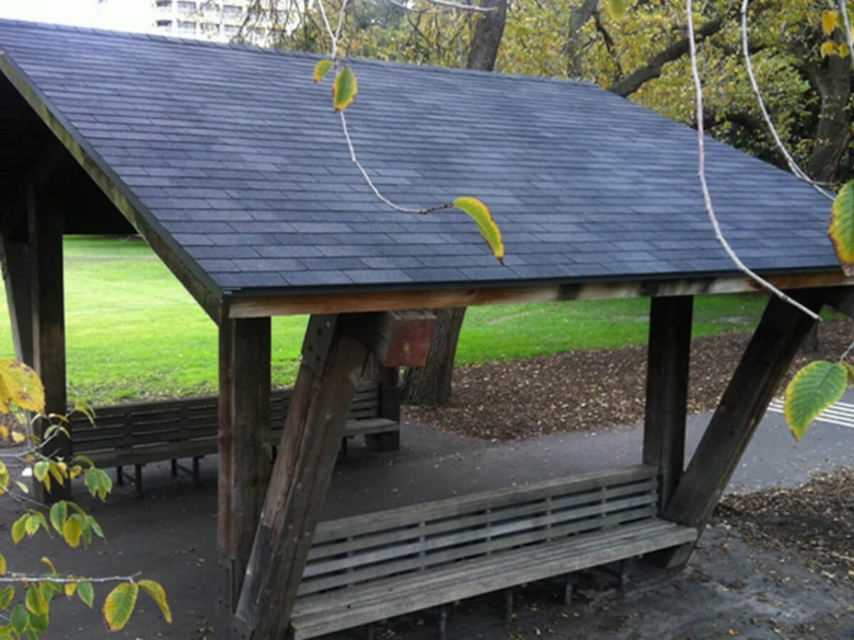 Střešní šindele na dřevěné konstrukci v parku jako příklad použití stavebního materiálu.