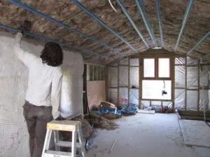 Muž instaluje střešní izolaci mezi trámy v nehotovém podkroví.