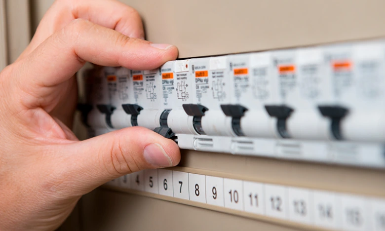 Ruka přepíná vypínače jističů v elektrickém rozvaděči.