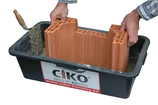 Ruční sestavení cihlového komína v nádobě s maltou.