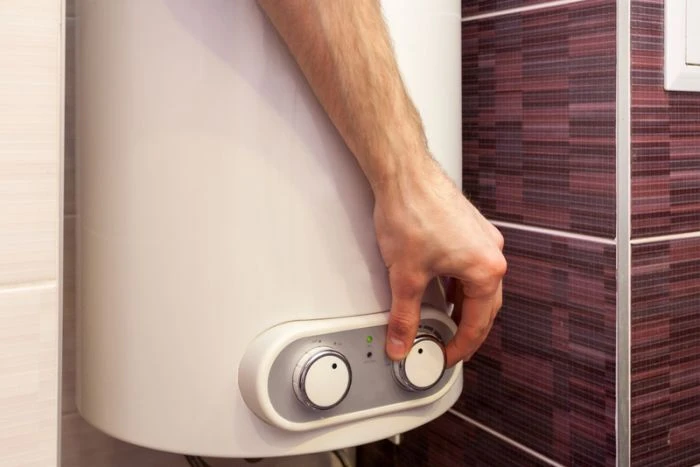 Ruka nastavuje teplotu na elektrickém bojleru v koupelně.