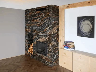 Moderní krb obložený tmavým mramorem s dřevěným nábytkem.