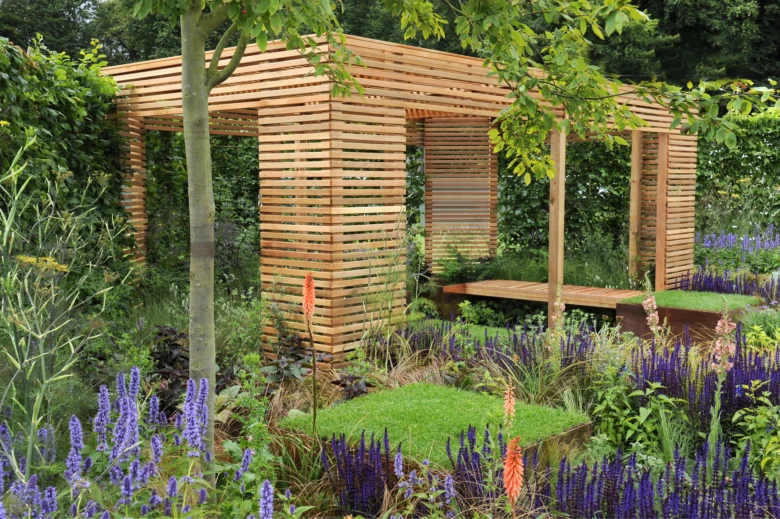 Moderní dřevěná pergola v zahradě s kvetoucími rostlinami.