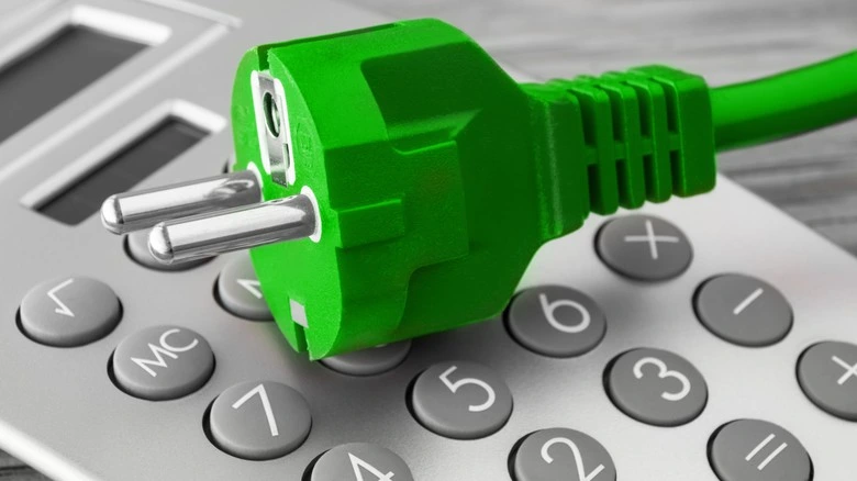 Zelená elektrická zástrčka na kalkulačce pro téma ceny elektřiny.