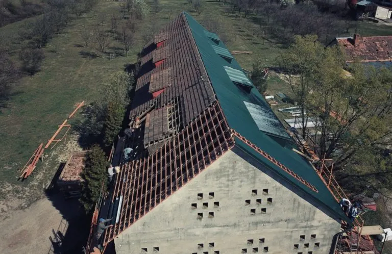 Stavebníci montují latě pod plechovou střechu s viditelnou roztečí.
