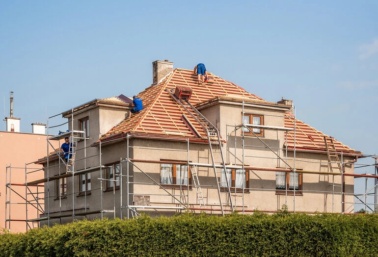 Stavebníci rekonstruují střechu domu s opěrným schodištěm.