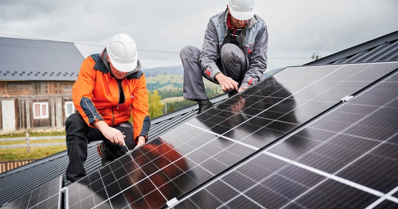 Dva pracovníci montují fotovoltaické panely na střechu rodinného domu.