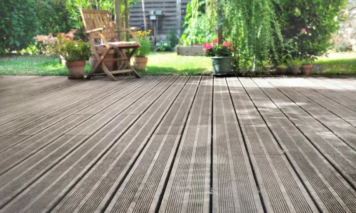 Dřevěná terasa u domu s židlí a kvetinami v zahradě.