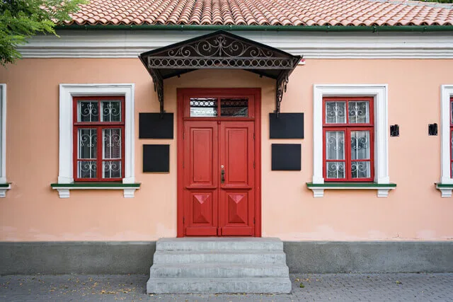 Černá kovová stříška nad červenými dveřmi na fasádě domu.
