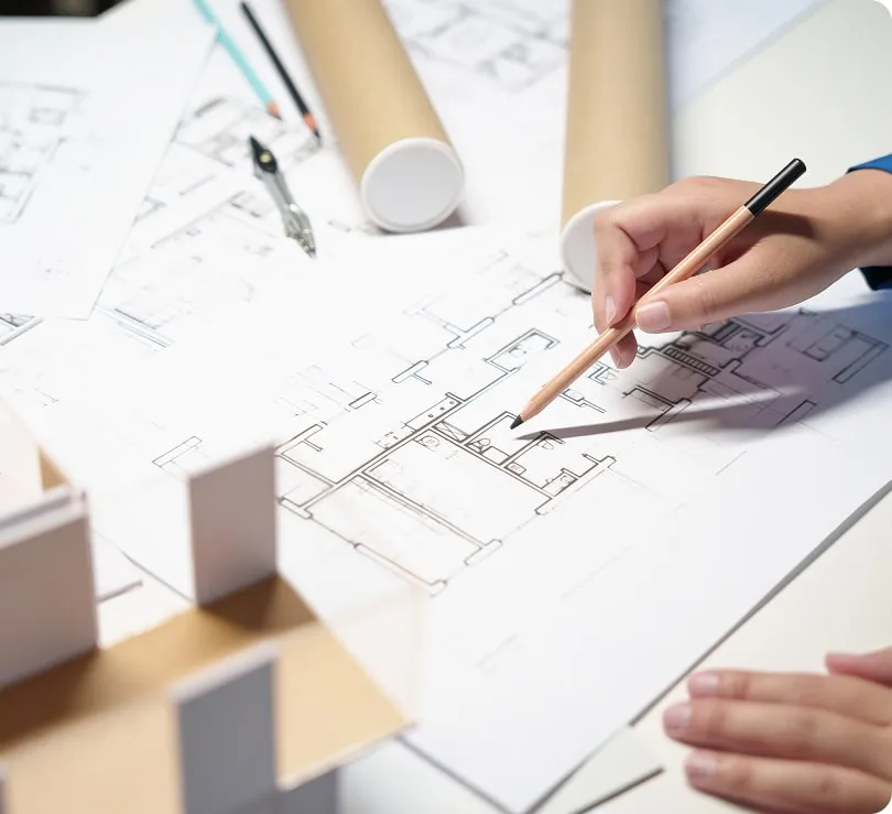 Architekt kreslí plán domu vedle modelu pro stavbu na klíč.