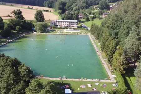 Venkovní bazén v Jeseníkách s plavci na pozadí lesa.