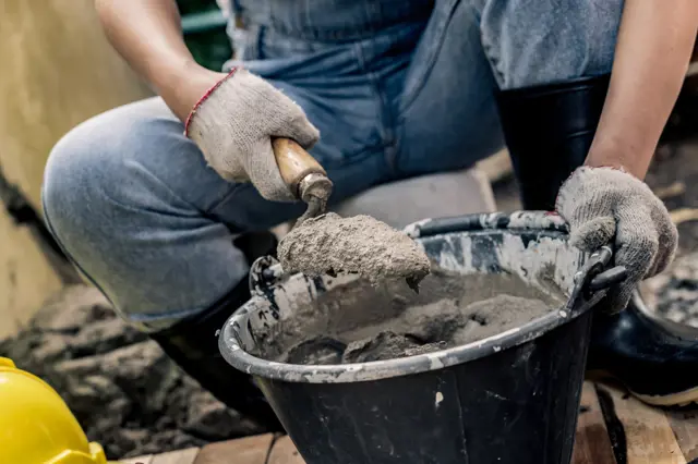 Stavebník míchá beton lopatkou z kbelíku na stavbě.