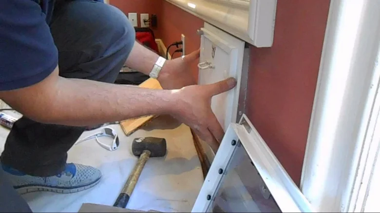 Muž montuje dvířko pro psa do dveří pomocí nástrojů.