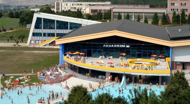 Vnější pohled na bazénový komplex Aquadrom v Mostě s lidmi ve vodě.