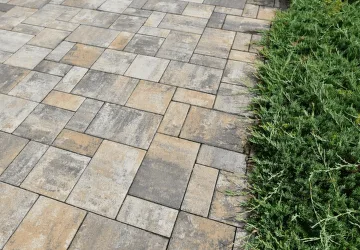 Betonová dlažba na terase s přírodními kameny vedle zelené trávy.