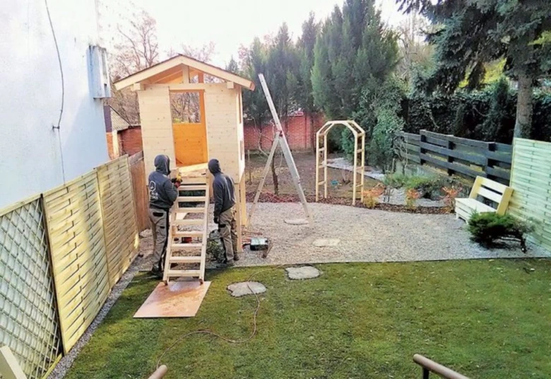 Dva muži staví dřevěný zahradní domek z palet v záhonu.