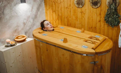 Žena v dřevěné vaně ve saunovém prostoru.