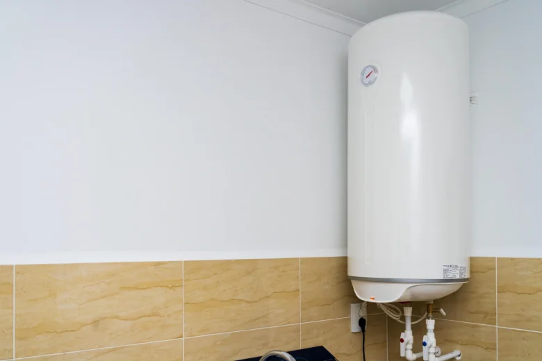 Bílý elektrický ohřívač vody na zdi v koupelně s hadicemi.