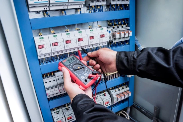 Elektrikář měří napětí v průmyslovém rozvaděči multimetrem.