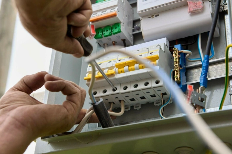 Elektrikář upravuje jističe v rozvaděči šroubovákem.