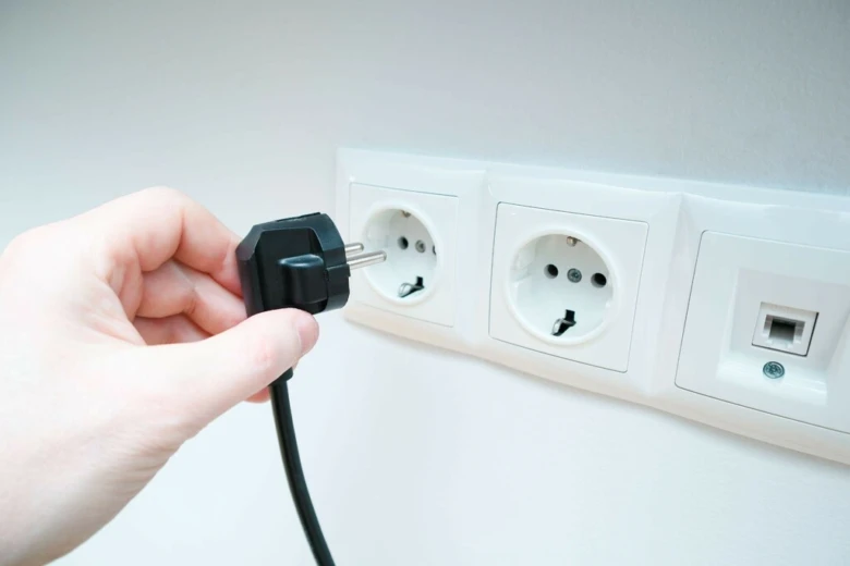 Ruka zapojuje černý elektrický zástrčku do zásuvky pro střídavý proud.