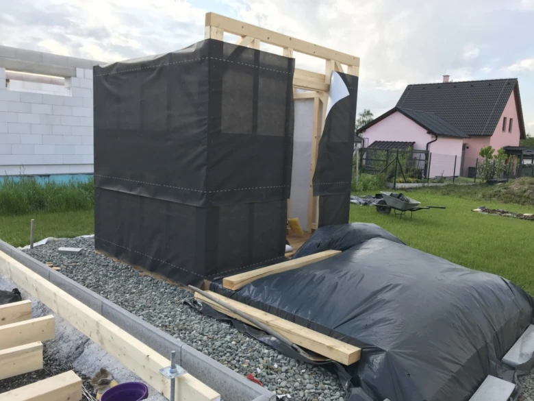 Stavba venkovní sauny z dřeva s černou fólií na zahradě.