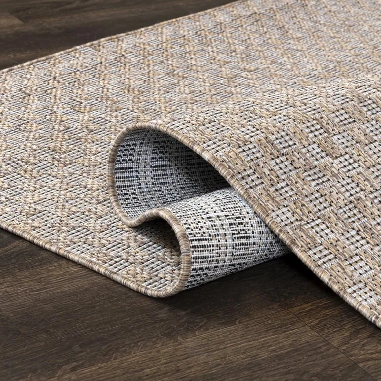 Detail texturovaného koberce položeného na dřevěné podlaze.