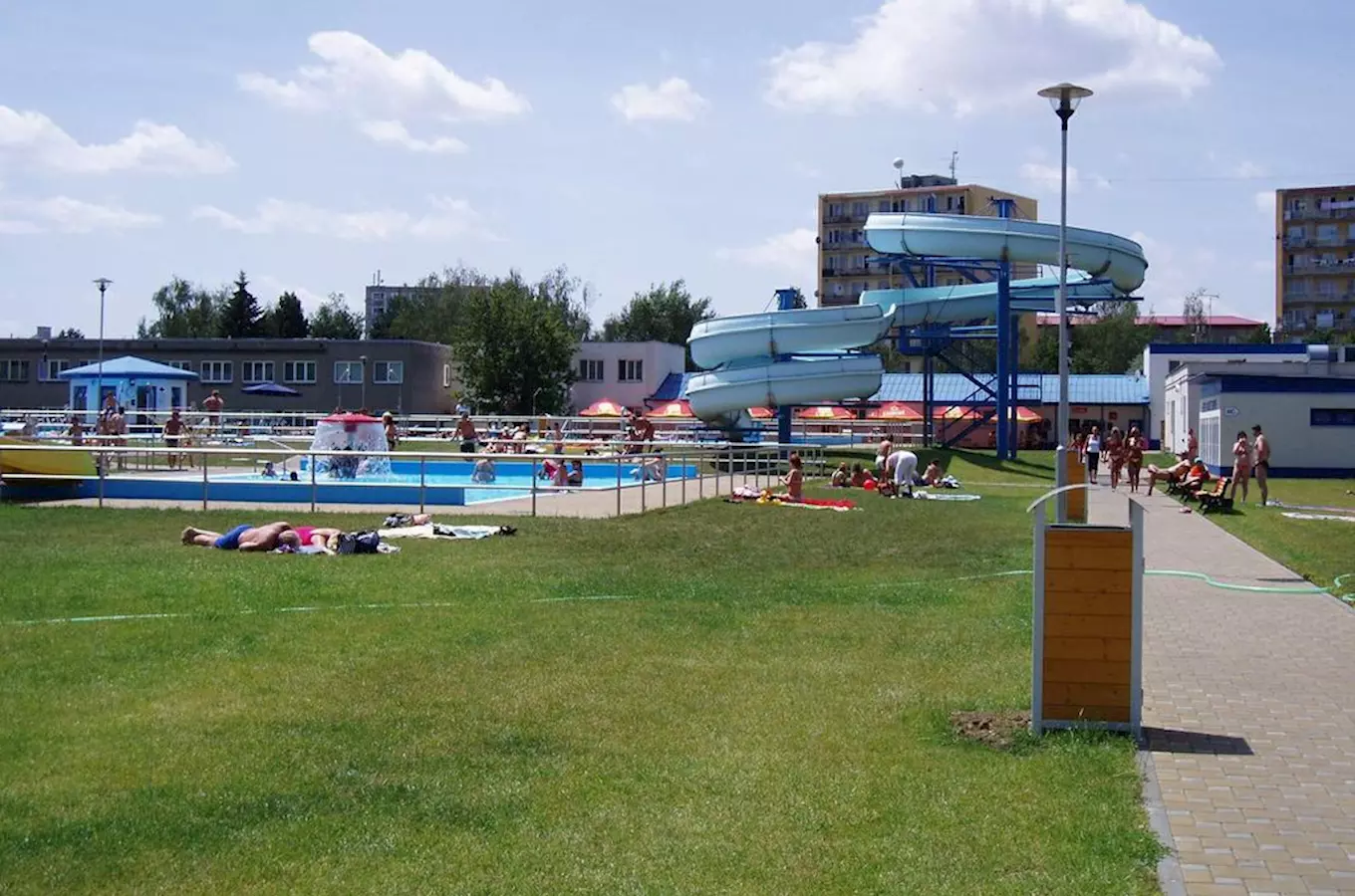 Venkovní bazén s vodními skluzavkami a slunečníky v koupališti.