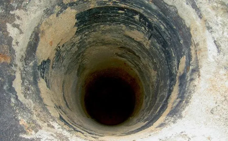 Hluboká šachta v technické instalaci s tmavým povrchem.