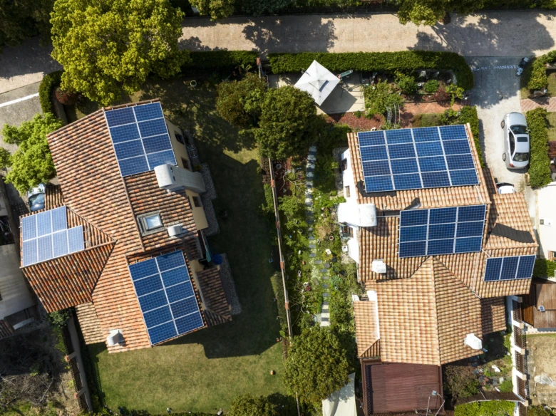 Dvě rodinné domy s fotovoltaickými panely na střechách zobrazené ze vzduchu.