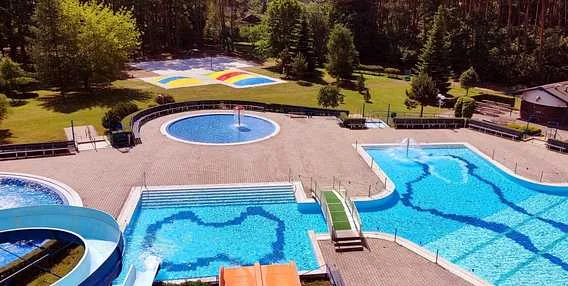 Vzdušný pohled na venkovní bazénový komplex s tobogány a barevnou uměleckou výzdobou.