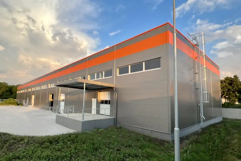 Moderní skladová hala s šedou fasádou a oranžovým pruhem.