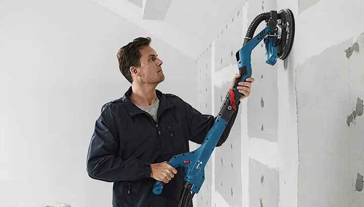 Muž hladí sádrokartonovou stěnu elektrickým nástrojem.