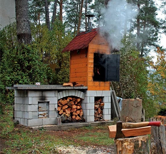 Hotová zděná udírna s dřevem a komínem v přírodě.
