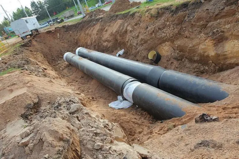 Dvě velké černé vodovodní trubice uložené v vykopaném příkopu.