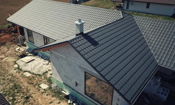 Montáž oplechování střechy s viditelnými závětními lištami na domě.