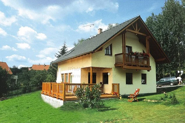 Dřevostavba na klíč s dřevěnou terasou v zelené trávě.