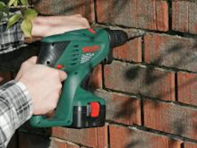 Osoba vrtá do cihlové zdi pomocí elektrického vrtače.