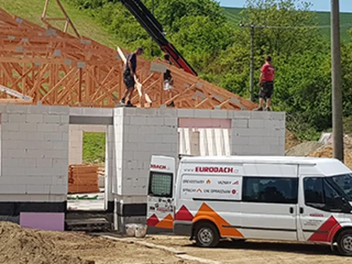 Stavební práce na domě s pracovníky a služebním vozem firmy.