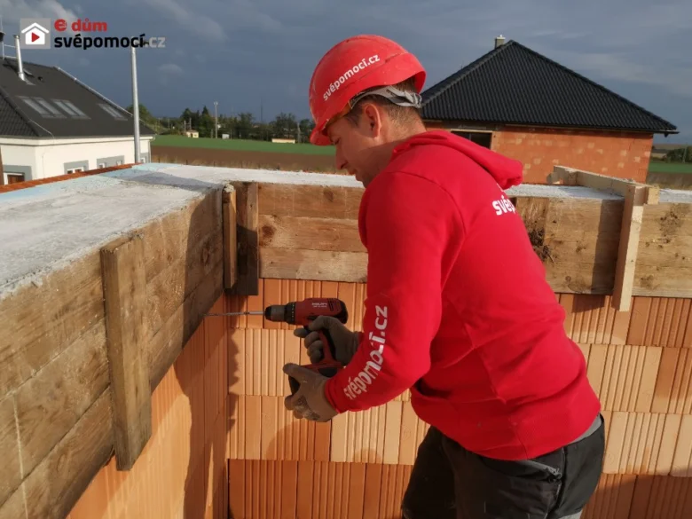 Stavebník montuje dřevěné bednění pro betonový věnec.