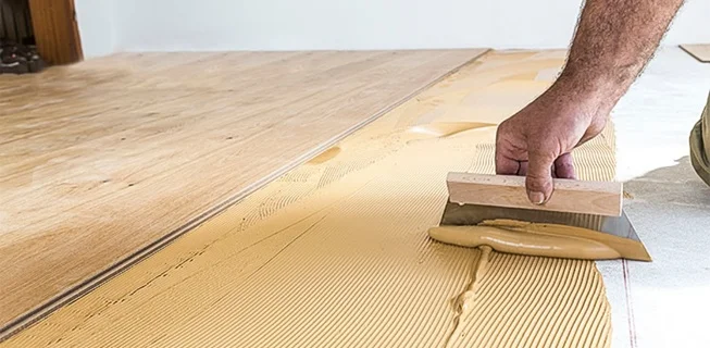 Ruka rozšiřuje lepidlo na podlahu před pokládkou vinylové dlažby.