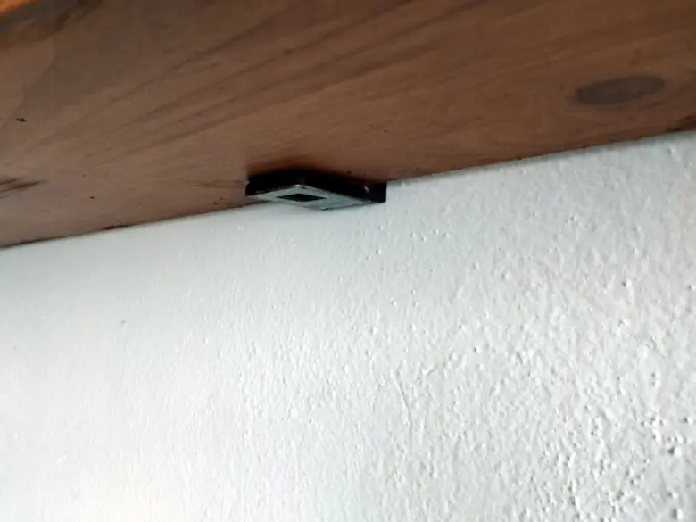Kuchyňská polička připevněná k zdi pomocí kovového držáku.