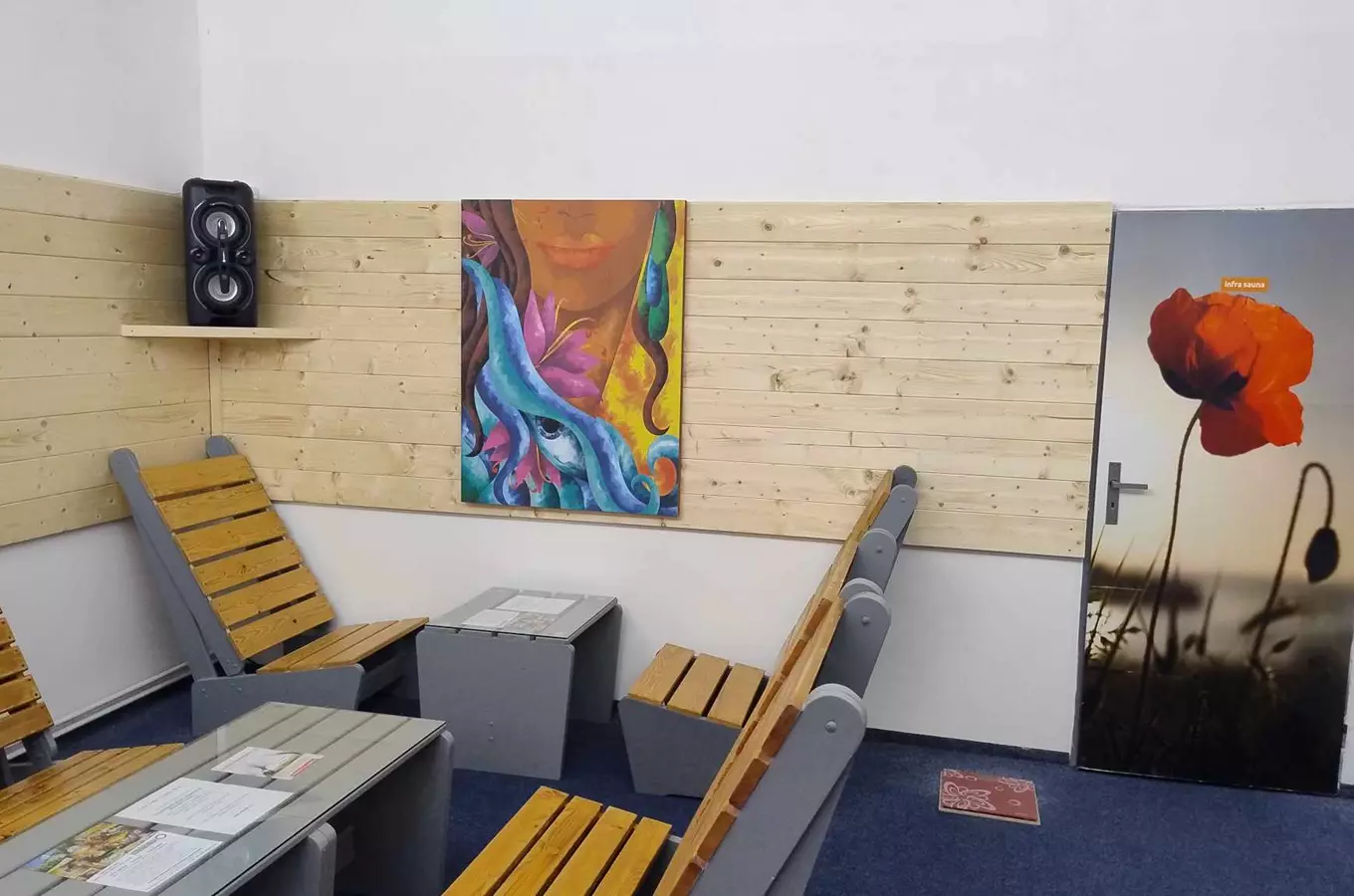 Vnitřek sauny s dřevěnými židlemi a barevnou malbou na zdi.