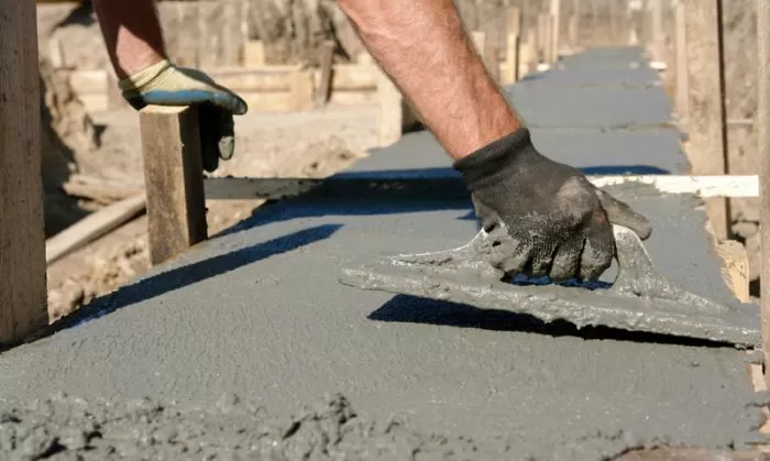 Stavebník hladí čerstvý beton na základu rukama s lopatkou.